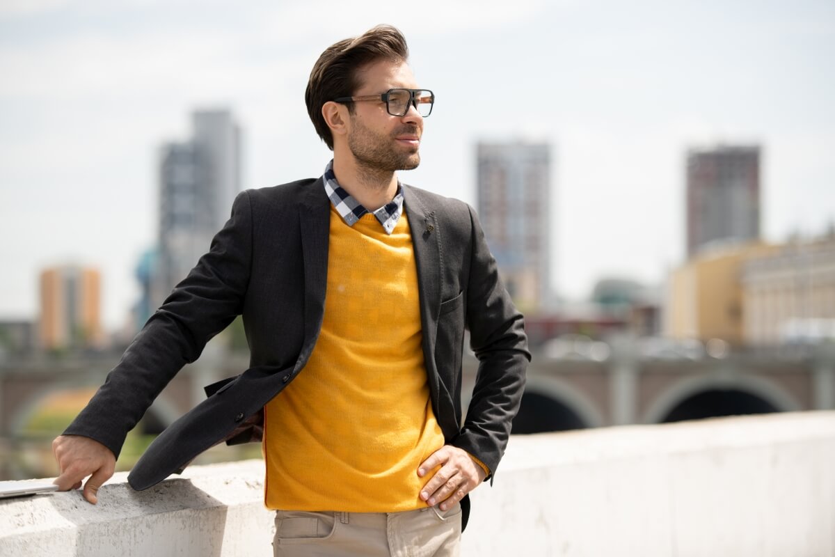 Mężczyzna ubrany w stylu smart casual męski, stoi na tle miasta.